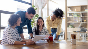 Three colleagues smiling around a table while reviewing paperwork.