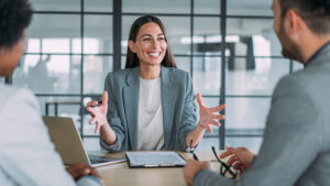 A happy female employee sitting at a table with a laptop and having an animated conversation.