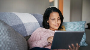 Female on sofa smiling and looking at a tablet.