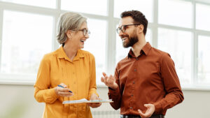 Male and female smiling and having discussion in an office setting.