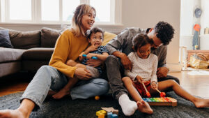 Family of four sitting on the floor in their home, playing, laughing and having a good time together.