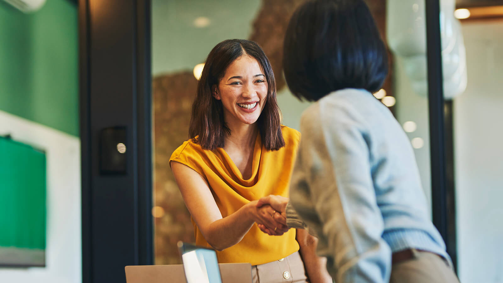 Two women smile and shake hands as they discuss their business partnership through a professional employer organization.