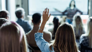 Woman raising her hand amid a group of people in a classroom.