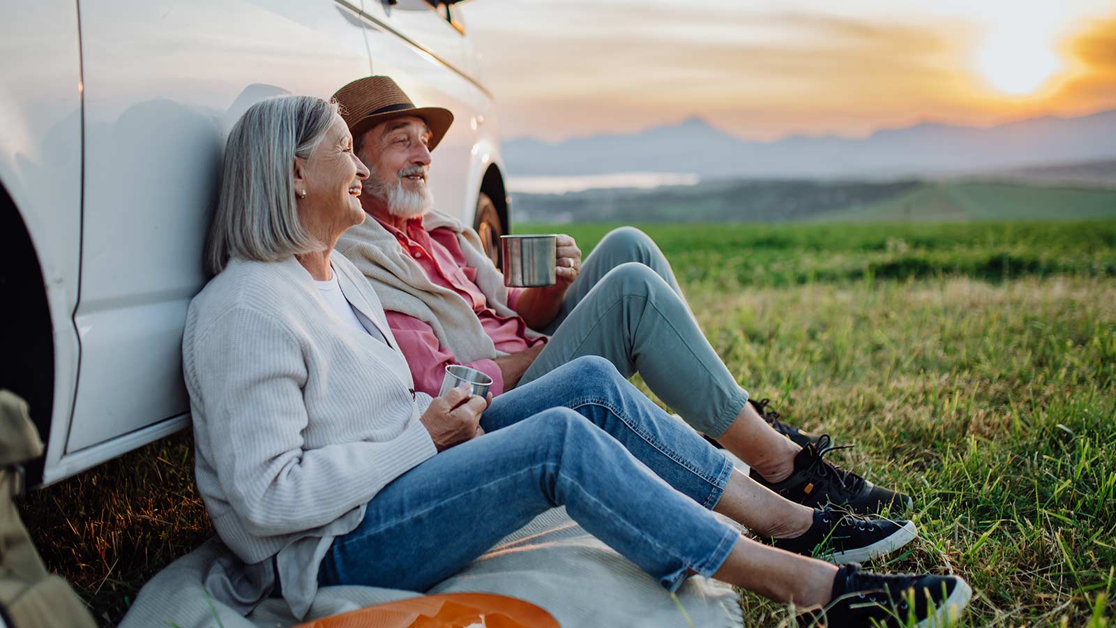 Elderly couple sitting on the ground against a truck enjoying the outdoors.