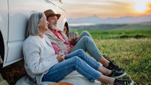 Elderly couple sitting on the ground against a truck enjoying the outdoors.