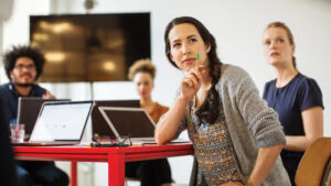 Several work associates with laptops sitting at a table in an office setting.