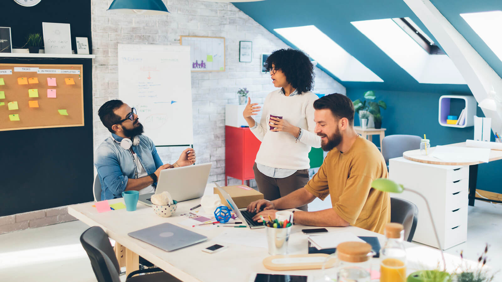 Three employees collaborate around a shared workspace in a modern, small-business office.