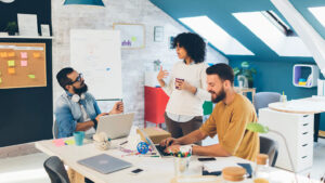 Three employees collaborate around a shared workspace in a modern, small-business office.