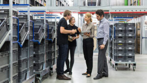 A business owner stands in her warehouse reviewing product information with three of her key employees.