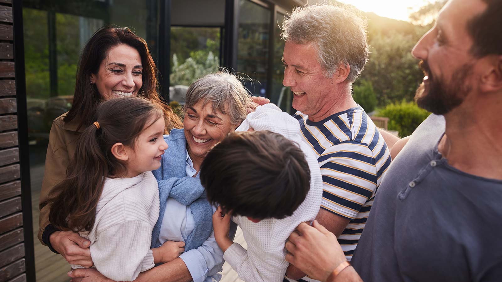 Grandparents greet their young grandson and granddaughter with enthusiastic hugs while the parents happily smile on the side.