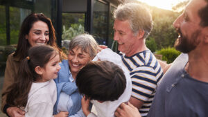 Grandparents greet their young grandson and granddaughter with enthusiastic hugs while the parents happily smile on the side.