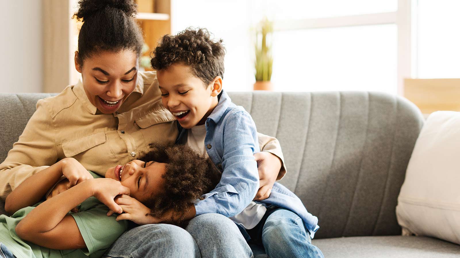 Mother hugging and laughing with two children on a sofa.