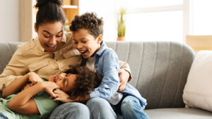 Mother hugging and laughing with two children on a sofa.