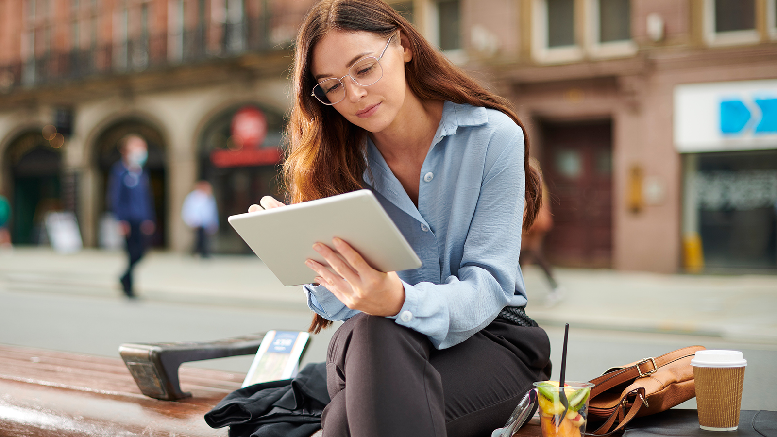 A young professional woman checks her credit score on her tablet while taking her lunch break on a bench outside.