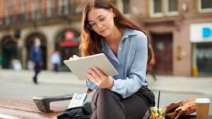 A young professional woman checks her credit score on her tablet while taking her lunch break on a bench outside.