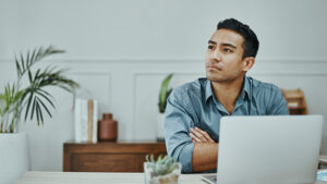 Young man in deep thought with open laptop.