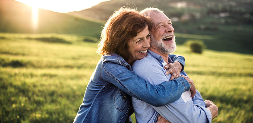 Elderly couple laughing, hugging and enjoying the outdoors.