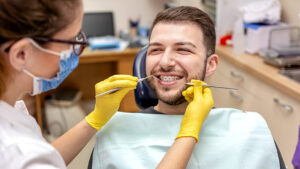 Young man smiling with braces while getting his teeth checked by the orthodontist assistant.